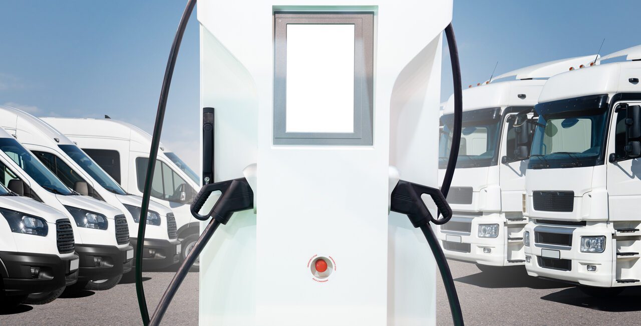 Electric vehicles charging station on a background of trucks and vans. Electric Vehicle Fleet Management concept.