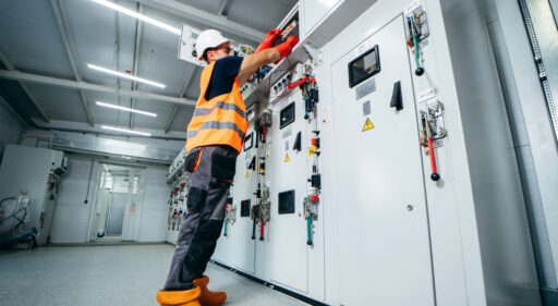 Adult electrician builder engineer testing and screwing equipment in fuse box and repairing of modern electricity power station using voltmeter. Automatic control cabinet